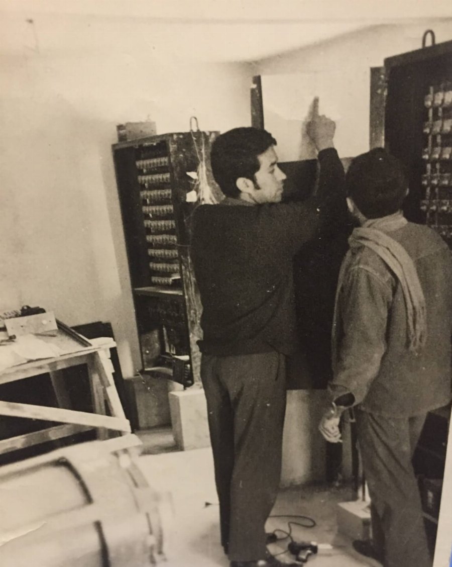 Foto antigua en blanco y negro de dos técnicos trabajando frente a un tablero de control de ascensores